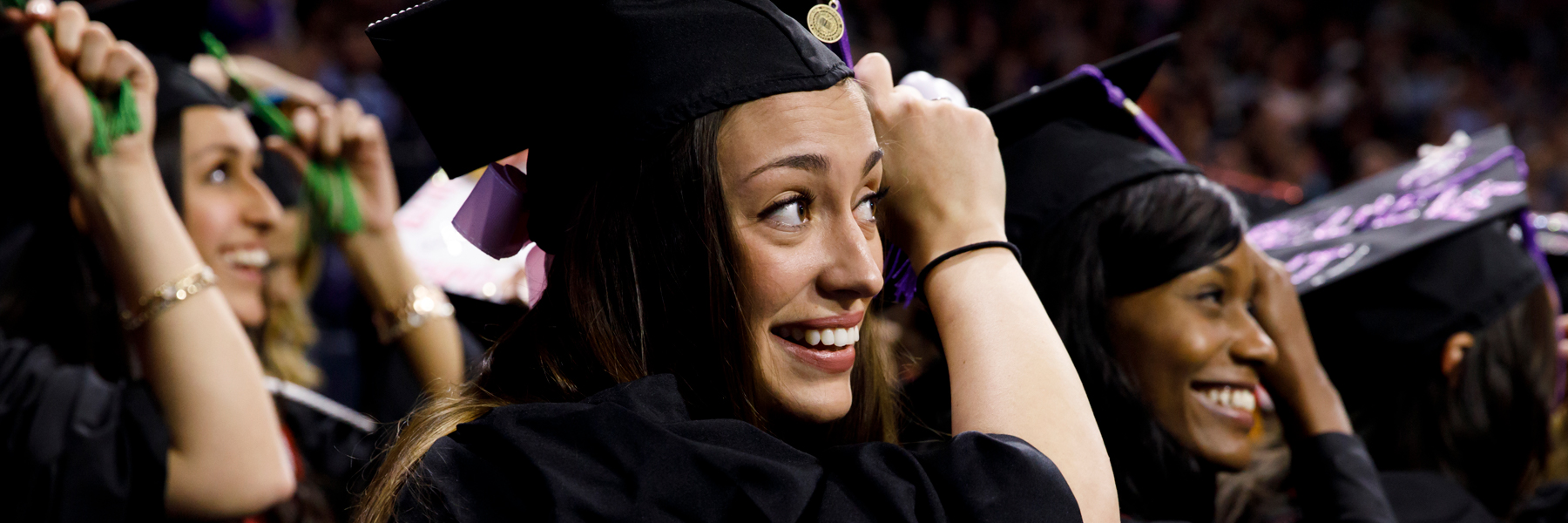 Graduating students prepare to switch their mortarboard tassels to the other side.